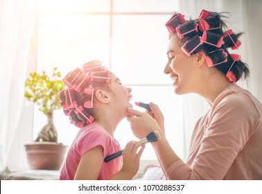 Happy Loving Family. Mother And Daughter Are Doing Hair And Having Fun. Mom Putting Lipstick On Her Child.