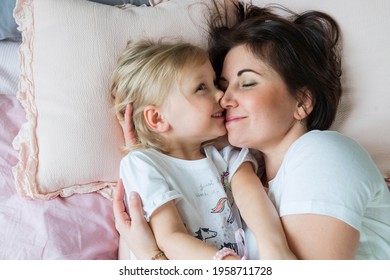 Happy Loving Family. Mother And Daughter Woke Up And Touching Noses To Nose In Bed. Woman, Toddler Girl In White T-shirts Enjoying In Bedroom. Pastime At Home, Comfort. Carefree Childhood. Mother Day