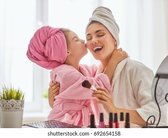 Happy loving family. Mother and daughter are doing make up and having fun sitting at dressing table at home. Mom and child girl are in bathrobes and with towels on their heads. - Powered by Shutterstock