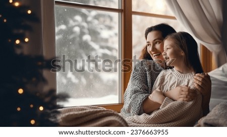 Happy loving family. Mother and daughter are hugging and enjoying winter nature in the  window.