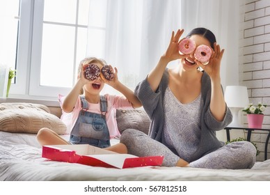 Happy Loving Family. Mother And Her Daughter Child Girl Are Eating Donuts And Having Fun On The Bed In The Room.