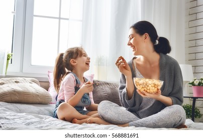 Happy loving family. Mother and her daughter child girl are eating popcorn on the bed in the room.