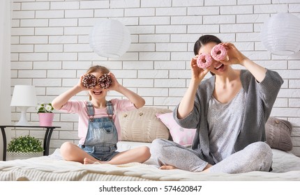 Happy Loving Family. Mother And Her Daughter Child Girl Are Eating Donuts And Having Fun On The Bed In The Room.