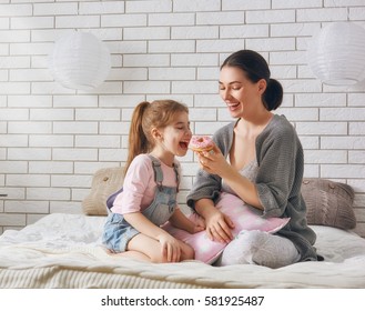 Happy loving family. Mother and her daughter child girl are eating donuts and having fun on the bed in the room.