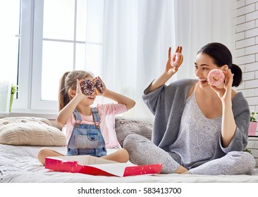 Happy Loving Family. Mother And Her Daughter Child Girl Are Eating Donuts And Having Fun On The Bed In The Room.