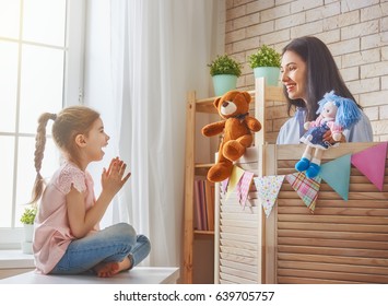 Happy loving family. Mother and her daughter in kids room. Funny mom and lovely child having fun and playing performance in the puppet theater indoors. Doll and teddy bear. - Powered by Shutterstock