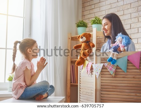 Happy loving family. Mother and her daughter in kids room. Funny mom and lovely child having fun and playing performance in the puppet theater indoors. Doll and teddy bear.