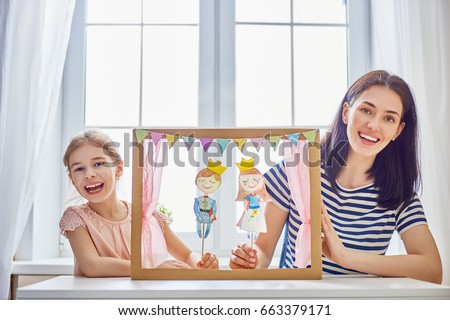 Happy loving family. Mother and her daughter in kids room. Funny mom and lovely child having fun and playing performance in the puppet theater indoors. Prince and princess.