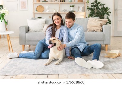 Happy Loving Family. Portrait of beautiful spouses patting dog sitting on the floor carpet in modern apartment