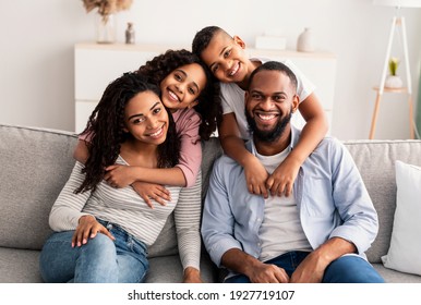 Happy Loving Family. Portrait of cheerful African American man and woman sitting on the couch at home, posing for photo, smiling boy and girl embracing parents from the back. Bonding