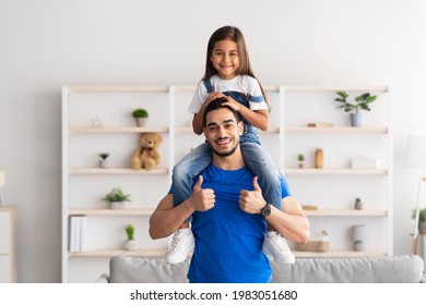 Happy Loving Family. Portrait Of Cheerful Man Riding Excited Daughter On Shoulders, Looking At Camera And Showing Thumb Up Sign Gesture, Having Fun, Celebrating Father's Day Standing In Living Room - Powered by Shutterstock