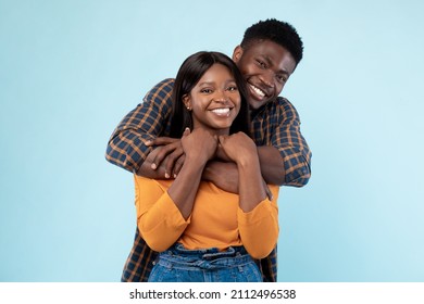 Happy Loving Family. Portrait Of Cheerful Black Couple Hugging At Blue Studio Background, Closeup. Smiling Young Man Embracing His Beautiful Girlfriend From Behind, Millennials Spending Time Together