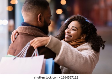 Happy Loving Family. Portrait Of Smiling African American Woman Embracing Her Man, Carrying Shopping Bags And Looking At Him While Walking Near Mall In The Evening, Black Couple Hugging