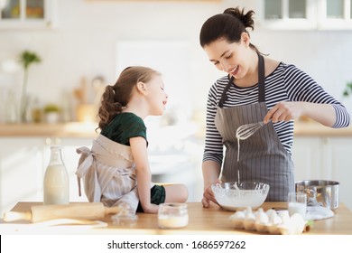Happy loving family are preparing bakery together. Mother and child daughter girl are cooking cookies and having fun in the kitchen. Homemade food and little helper.                                
