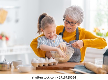 Happy loving family are preparing bakery together. Granny and child are cooking cookies and having fun in the kitchen. 