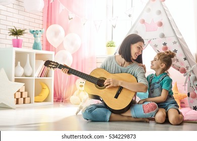 Happy Loving Family. Pretty Young Mother And Daughter Playing Guitar Together. Adult Woman Playing Guitar For Child Girl Indoors. Funny Mom And Lovely Child Having Fun In Children Room.