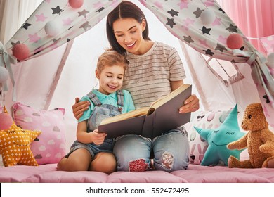 Happy Loving Family. Pretty Young Mother Reading A Book To Her Daughter Indoors. Funny Mom And Lovely Child Having Fun In Children Room.