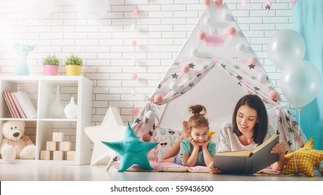 Happy Loving Family. Pretty Young Mother Reading A Book To Her Daughter Indoors. Funny Mom And Lovely Child Having Fun In Children Room.