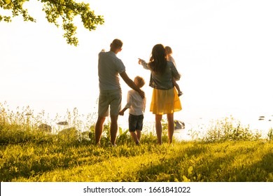 Happy Loving Family Walking Outdoor In The Light Of Sunset. Father, Mother, Son And Daughter.