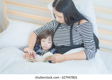 Happy Loving Family Young Asian Mother Reading A Bed Time Story Book To Her Daughter In Bedroom