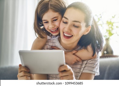 Happy loving family. Young mother and her daughter girl play in kids room. Funny mom and lovely child are having fun with tablet.