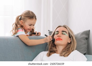 Happy Loving Family. Young Mother Sleeping On Sofa At Home While Child Girl Paint Face Colored Watercolors.Funny Make Up.having Fun.Prank