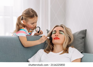 Happy Loving Family. Young Mother Sleeping On Sofa At Home While Child Girl Paint Face Colored Watercolors.Funny Make Up.having Fun.Prank