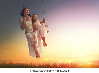 Happy loving family! Young mother and her child daughter swinging on the swings and laughing a summer evening outdoors. - Powered by Shutterstock