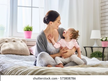 Happy loving family. Young mother are playing with her baby girl in the bedroom. Mom and child are having fun on the bed. - Shutterstock ID 573808786