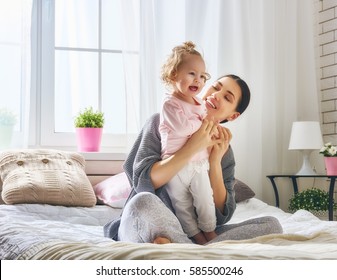 Happy Loving Family. Young Mother Are Playing With Her Baby Girl In The Bedroom. Mom And Child Are Having Fun On The Bed.