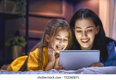 Happy Loving Family. Young Mother And Her Daughter Girl Are Playing In Bedroom. Funny Mom And Lovely Child Are Having Fun With Tablet.