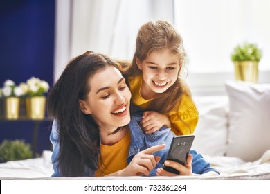 Happy Loving Family. Young Mother And Her Daughter Girl Are Playing In Bedroom. Funny Mom And Lovely Child Are Having Fun With Phone.