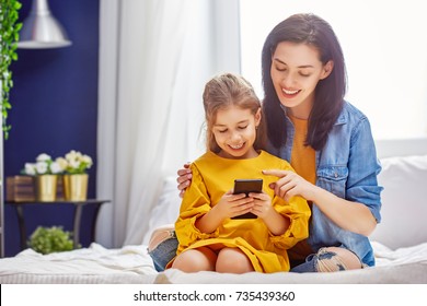 Happy Loving Family. Young Mother And Her Daughter Girl Are Playing In Bedroom. Funny Mom And Lovely Child Are Having Fun With Phone.