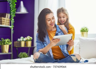 Happy Loving Family. Young Mother And Her Daughter Girl Are Playing In Bedroom. Funny Mom And Lovely Child Are Having Fun With Tablet.