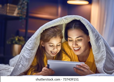 Happy Loving Family. Young Mother And Her Daughter Girl Are Playing In Bedroom. Funny Mom And Lovely Child Are Having Fun With Tablet.