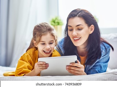 Happy Loving Family. Young Mother And Her Daughter Girl Are Playing In Bedroom. Funny Mom And Lovely Child Are Having Fun With Tablet.