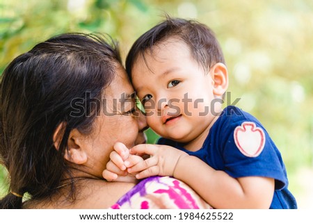 Happy loving family.Indian Grandmother and grandson are having a good time together and playing peekaboo and kiss her grandson outdoor.mixrace boy smiling laughing with his mother.Kid boy child.