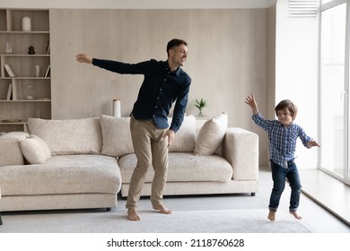 Happy loving father with little son dancing in living room, moving to music at home together, smiling young dad with 6s boy child having fun engaged in funny activity, spending leisure time