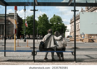 Happy, loving, hugging pensioners, elderly man and woman, sitting at bus stop in Berlin capital of Germany, looking at city street. Photography, tourism concept. - Powered by Shutterstock