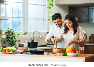 Happy loving Indian asian young couple cooking food in kitchen together, hugging, standing at table - Powered by Shutterstock