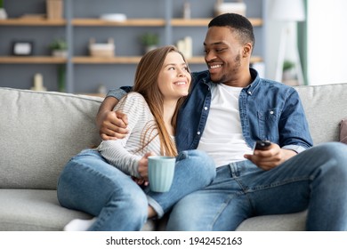 Happy loving interracial couple relaxing at home, watching tv and drinking coffee - Powered by Shutterstock