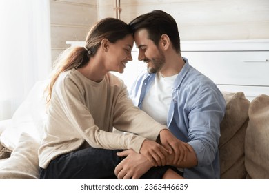 Happy loving man and woman enjoying tender moment with closed eyes, touching foreheads, expressing unity and care, beautiful girlfriend sitting on boyfriend laps, relaxing on cozy couch at home - Powered by Shutterstock