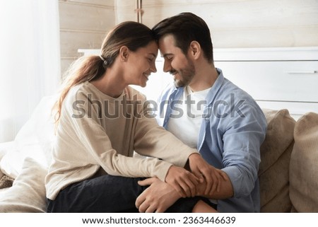 Happy loving man and woman enjoying tender moment with closed eyes, touching foreheads, expressing unity and care, beautiful girlfriend sitting on boyfriend laps, relaxing on cozy couch at home