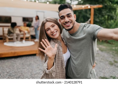 Happy loving multiracial couple taking selfie near camper van, resting with friends outdoors, free space. Arab guy and his girlfriend having fun summer camping trip, making mobile photo - Powered by Shutterstock