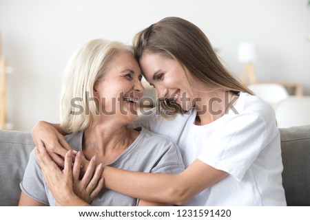 Happy loving older mature mother and grown millennial daughter laughing embracing, caring smiling young woman embracing happy senior middle aged mom having fun at home spending time together