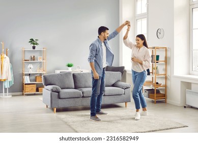 Happy loving romantic couple dancing together in living room. Full length shot of attractive young woman and man celebrating relocation, anniversary or enjoying spending time together at home - Powered by Shutterstock