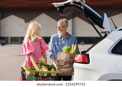 Happy loving senior couple doing shopping together, standing by car at parking spot next to mall, loading purchases grocery into automobile trunk, man and woman running errands on weekend - Powered by Shutterstock