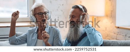 Happy loving senior couple having fun together, listening to the music in headphones, karaoke. Mature man and woman using modern technologies, active life. Concept of pensioner leisure time. Banner