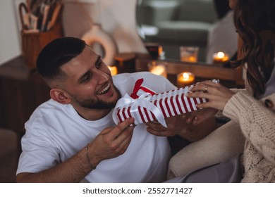 Happy loving young beautiful couple exchanging gift boxes for Christmas, new year or saint Valentine's Day. Man and woman in casual clothes holding presents, smiling, enjoying holidays at home - Powered by Shutterstock