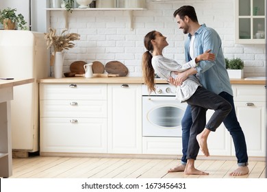 Happy loving young couple dancing romantic dance on date in modern kitchen, smiling husband and wife celebrating anniversary, enjoying tender moment, having fun, moving to music at home